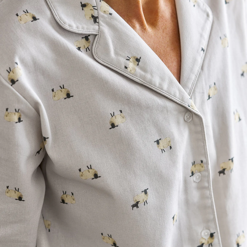 Close-up of a light gray pajama shirt with small sheep print on a neutral background