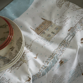Table setting with plates and a decorative tea towel featuring house and tree patterns.