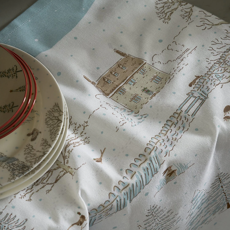 Table setting with plates and a decorative tea towel featuring house and tree patterns.