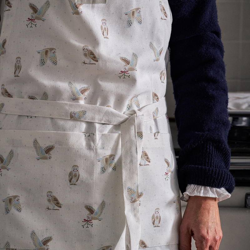 Person wearing a white apron with owl patterns in a kitchen setting