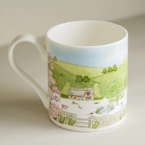 A white fine bone china mug with a spring cottage scene design, including a cottage, blossoming trees, and baby animals.