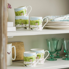 A white fine bone china mug with a spring cottage scene design, including a cottage, blossoming trees, and baby animals.