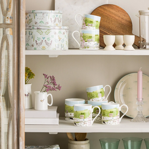 A white fine bone china mug with a spring cottage scene design, including a cottage, blossoming trees, and baby animals.