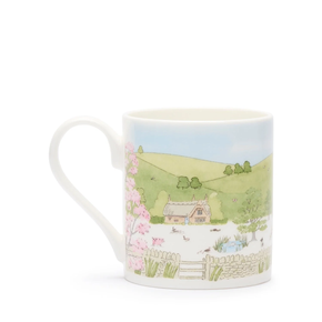 A white fine bone china mug with a spring cottage scene design, including a cottage, blossoming trees, and baby animals.