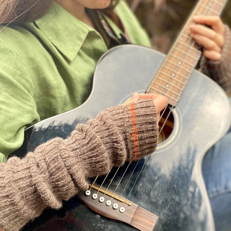 Person playing an acoustic guitar wearing brown wrist warmers with an orange stripe