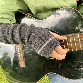 Person playing an acoustic guitar with a blurred natural background, wearing grey wrist warmers with lighter grey stripe
