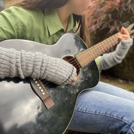 Person playing an acoustic guitar outdoors wearing grey wrist warmers