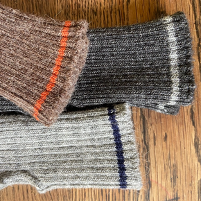 Three pairs of knitted wrist warmers in different colors on a wooden surface