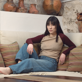 Woman sitting on a couch with decorative pillows and pottery in the background