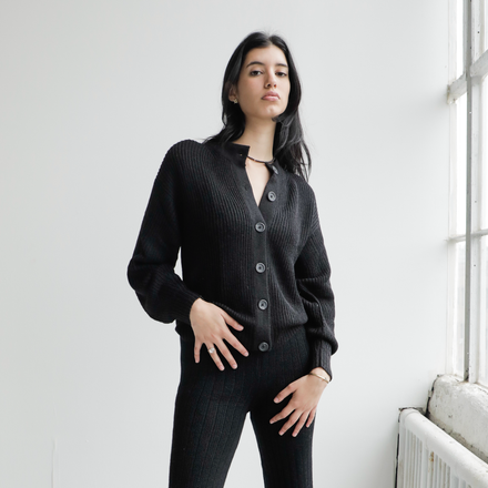 Woman wearing a black cardigan standing in a room with a white wall and window.
