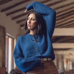 Woman wearing a blue sweater and brown pants indoors.
