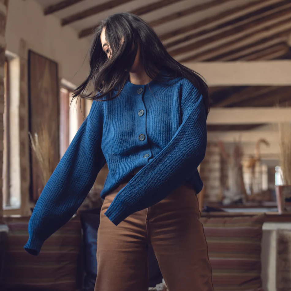 Person wearing a blue sweater and brown pants in an indoor setting with wooden beams.