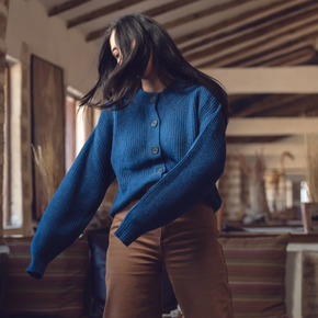 Person wearing a blue sweater and brown pants in an indoor setting with wooden beams.