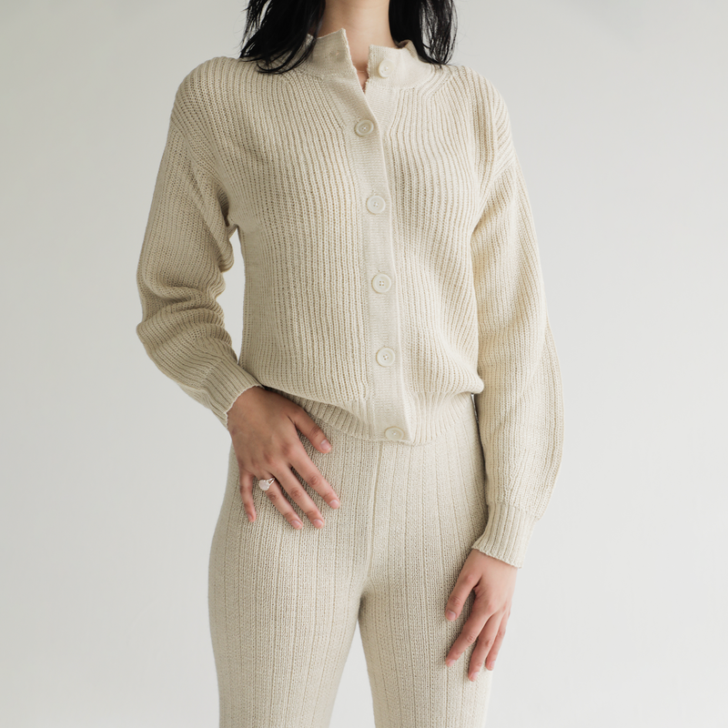 Person wearing a cream ribbed knit outfit on a plain background