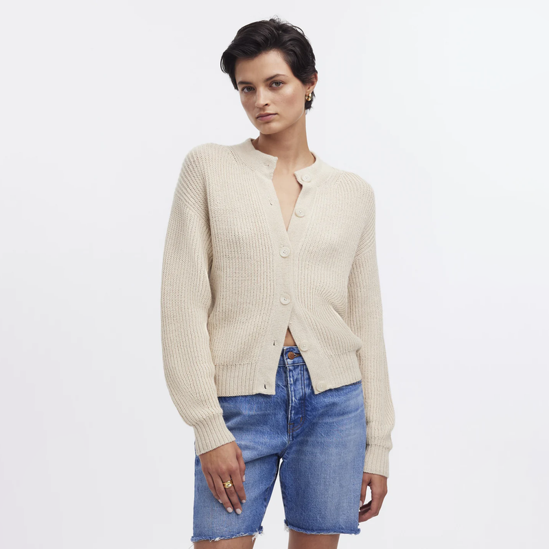 Woman wearing a cream cardigan and blue shorts on a light gray background