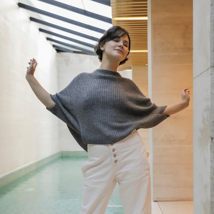 Woman wearing a gray sweater and white pants in an indoor setting with a striped ceiling.