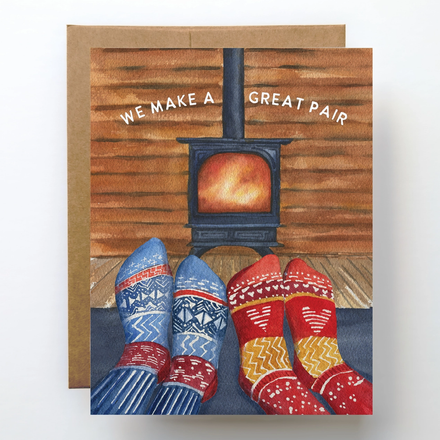 Card with illustration of feet in colorful socks by a wood stove, text 'WE MAKE A GREAT PAIR'.