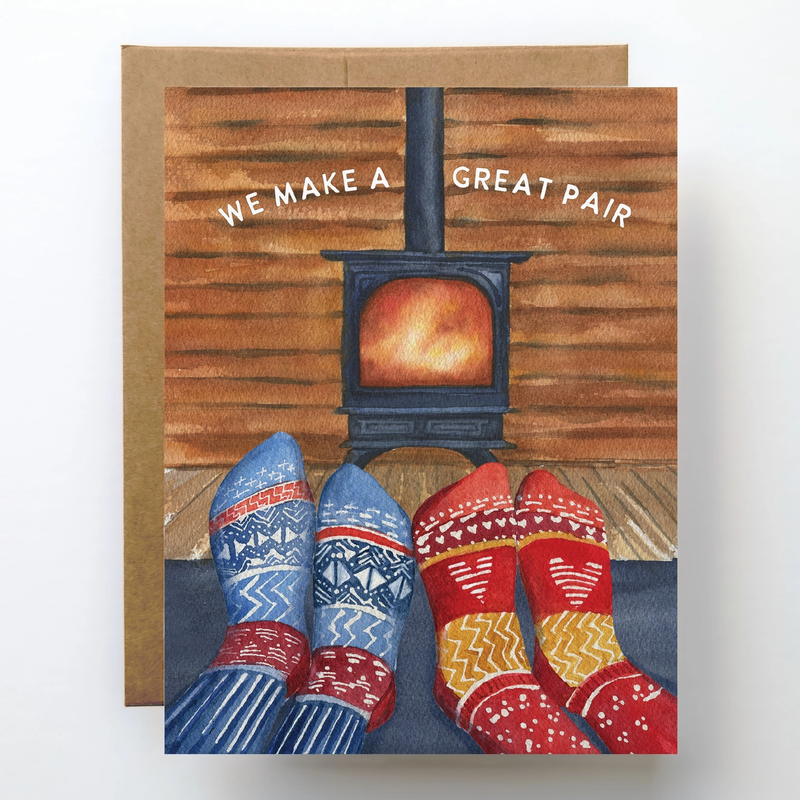 Card with illustration of feet in colorful socks by a wood stove, text 'WE MAKE A GREAT PAIR'.