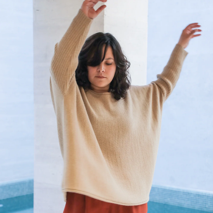 Woman wearing a white sweater with arms raised against a light blue background