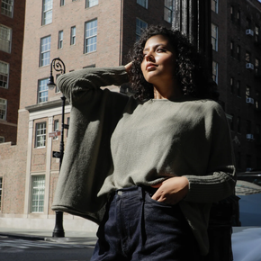 Woman in a green sweater and dark pants standing on a city street.