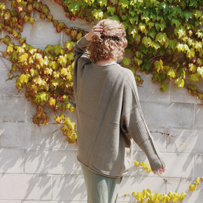 Person wearing a green sweater standing against a wall with ivy