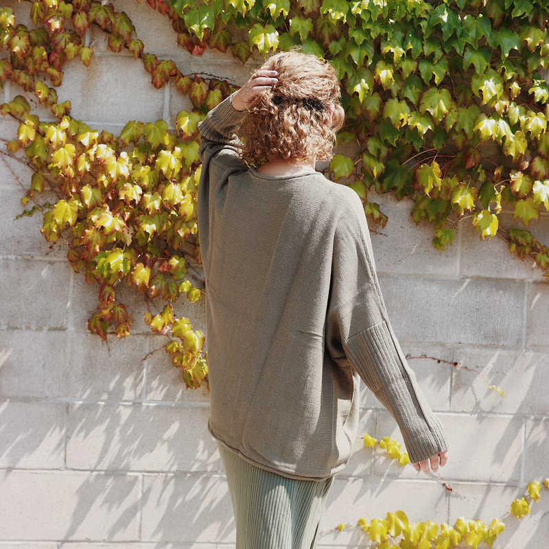 Person wearing a green sweater standing against a wall with ivy