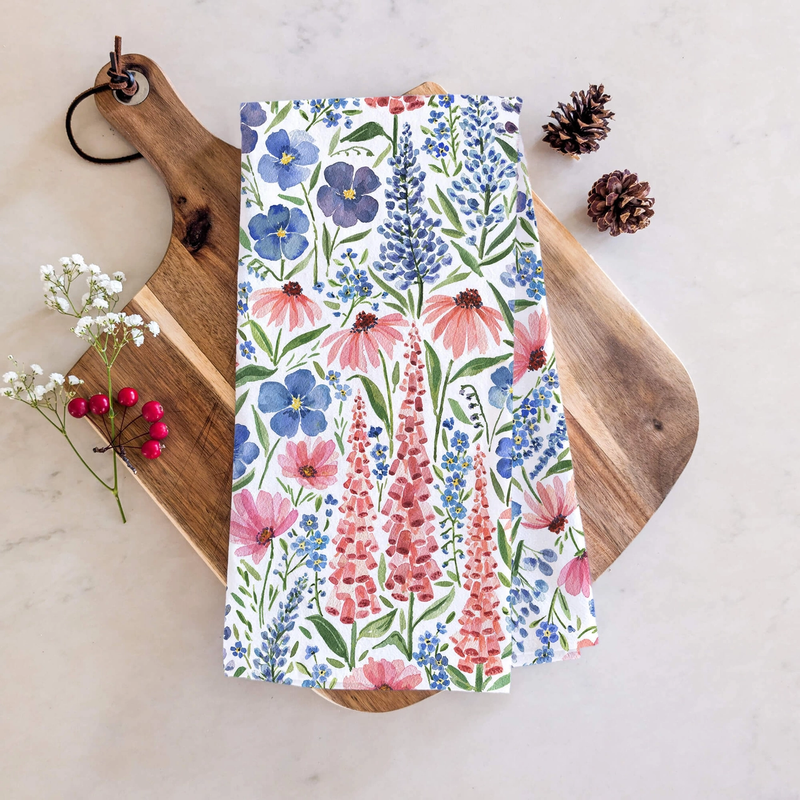 Floral patterned towel on a wooden cutting board with pine cones and flowers.