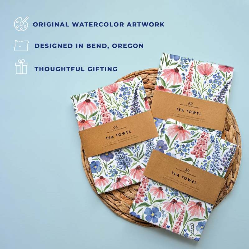 Floral tea towels with brown paper packaging on a woven basket against a light blue background.