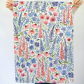 Floral patterned tea towel held by hands against a light gray background