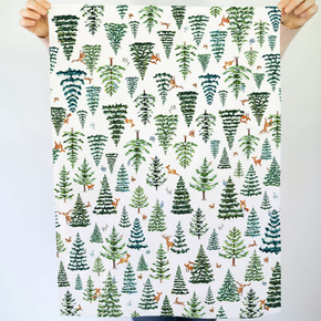 Patterned tea towel with trees and animals held by two hands against a light background