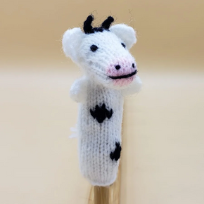 Knitted cow finger puppet on a wooden stick against a beige background