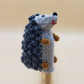 Knitted hedgehog finger puppet on a stick against a beige background