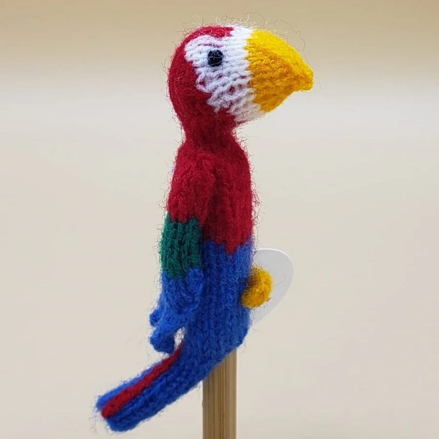 Knitted parrot finger puppet on a stick against a beige background
