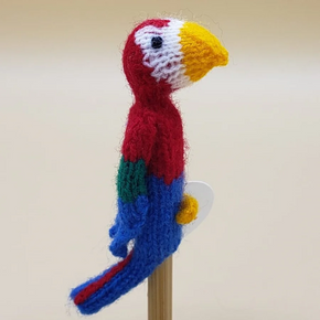 Knitted parrot finger puppet on a stick against a beige background