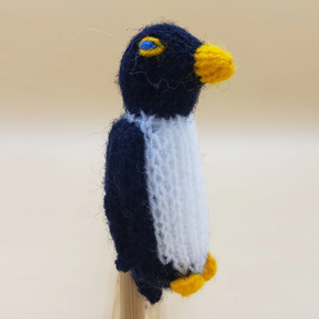 Knitted penguin finger puppet with black, white, and yellow colors on a beige background