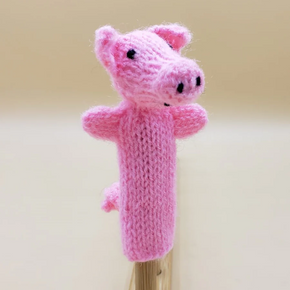Knitted pink pig finger puppet on a wooden stand against a beige background