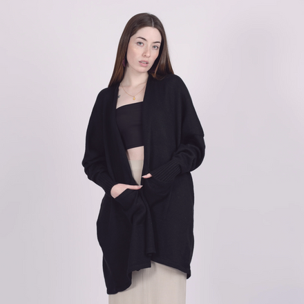 Woman wearing a black cardigan over a black top and beige pants on a white background