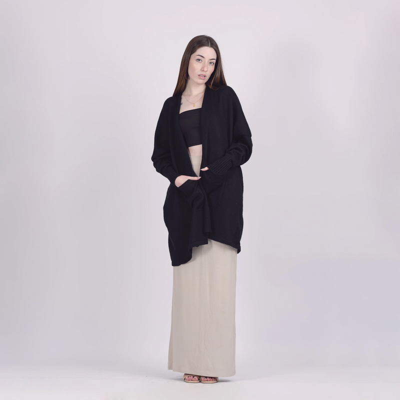 Woman wearing a black cardigan over a black top and beige pants on a white background