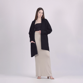 Woman wearing a black cardigan over a black top and beige skirt on a white background