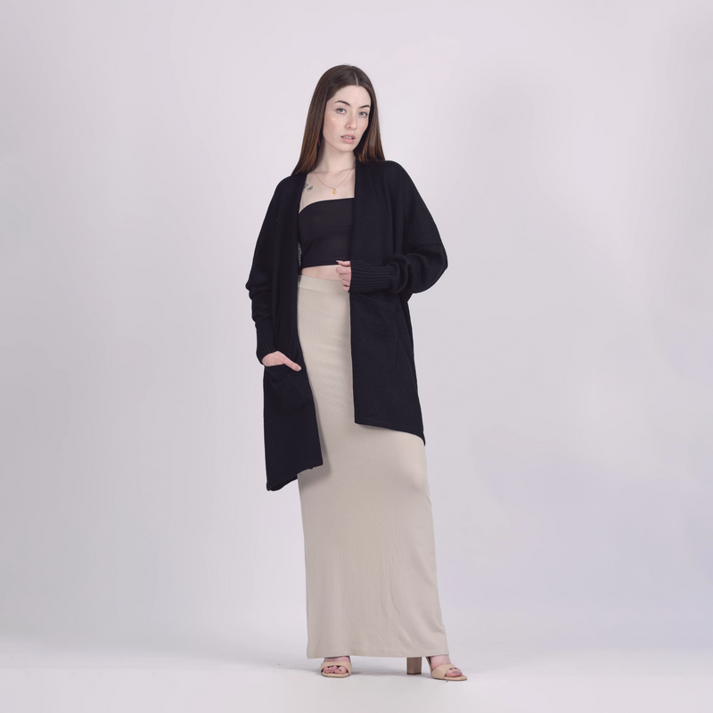 Woman wearing a black cardigan over a black top and beige skirt on a white background