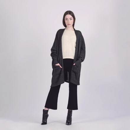 Woman wearing a long dark gray cardigan over a white top and black pants on a light gray background