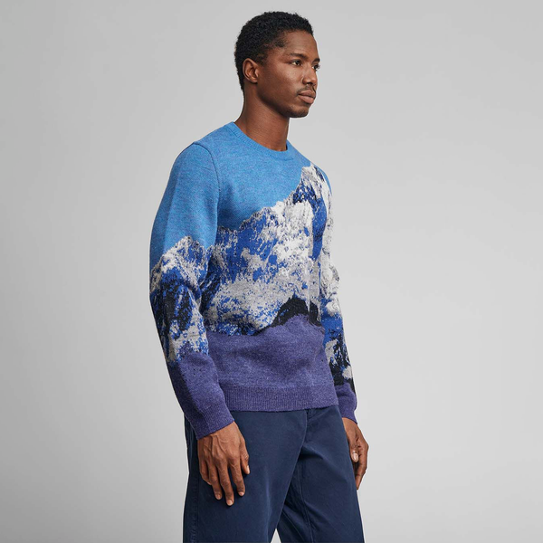 Kuna Huarascan Sweater - model wearing light blue and dark blue sweater with mountain range on a neutral background