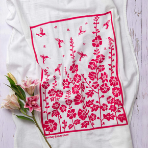 White dish towel with pink floral and bird pattern on a light wooden surface with flowers.