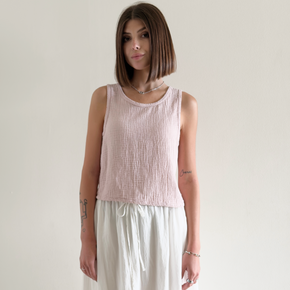 Woman wearing a light pink sleeveless top and white pants against a plain background