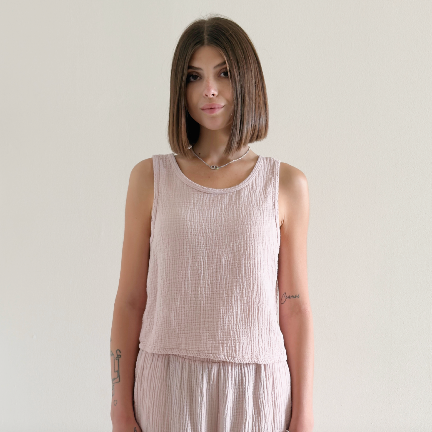 Woman wearing a light pink sleeveless top and pants against a plain background