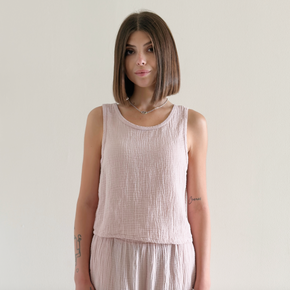 Woman wearing a light pink sleeveless top and pants against a plain background