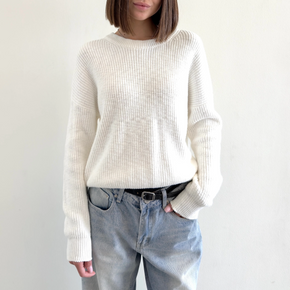 Person wearing a white sweater and light blue jeans against a plain background