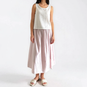 Woman wearing a white sleeveless top and light pink skirt on a white background