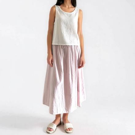 Woman wearing a white sleeveless top and light pink skirt on a white background