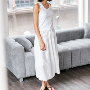 Woman in a white sleeveless top and skirt standing in a room with a gray sofa.